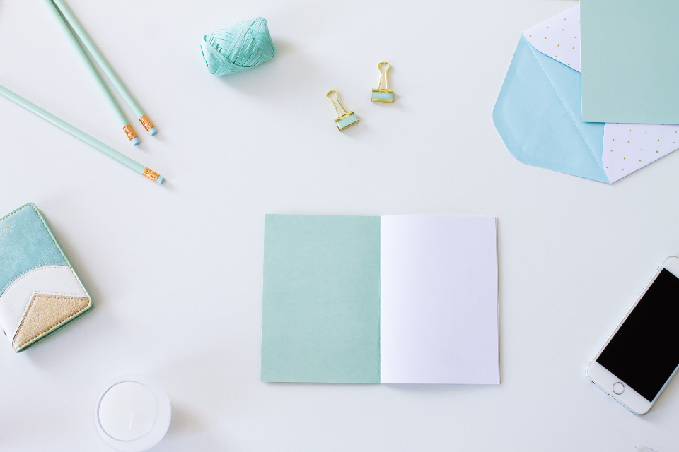 A mint notebook, pencils and a smartphone on a white desk