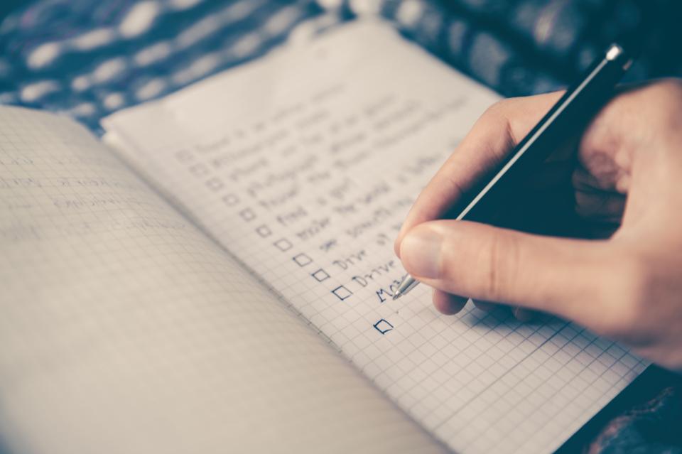 A hand writing a checklist in a grid-paper notebook