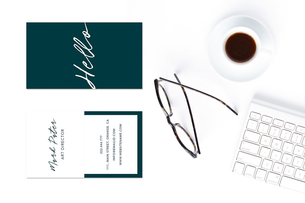 Business cards, a cup of coffee, glasses and a keyboard on a white desk