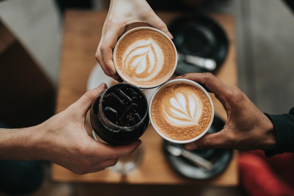 Three people raising coffee cups with latte art over a cafe table