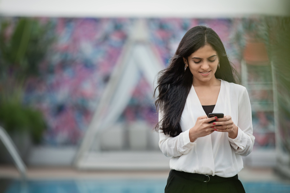 A smiling woman in a white blouse typing on her phone